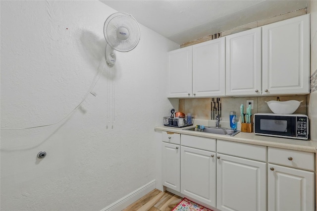 8525 N Ola Ave, Tampa, FL 33604 - kitchen featuring black microwave, a sink, light wood-style flooring, and white cabinetry