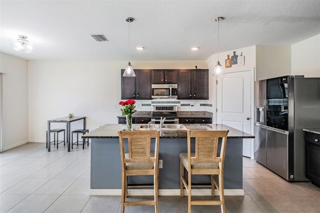 30989 Summer Sun Loop, Wesley Chapel, FL 33545 - kitchen with appliances with stainless steel finishes, light tile patterned flooring, dark brown cabinetry, an island with sink, and dark stone counters