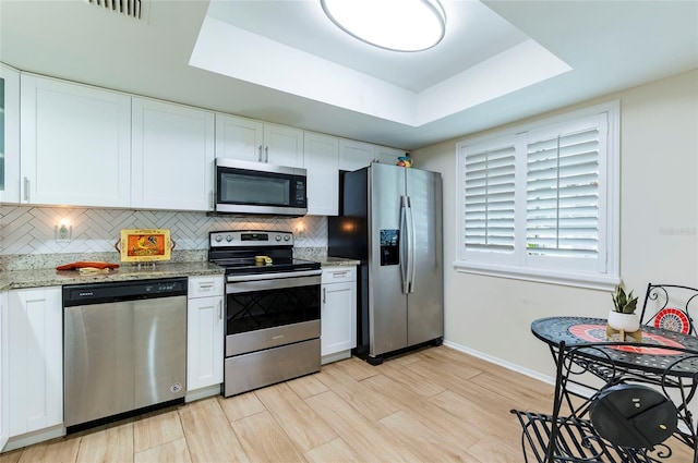 2238 Lark Cir W Unit D, Palm Harbor, FL 34684 - kitchen featuring appliances with stainless steel finishes, a raised ceiling, tasteful backsplash, baseboards, and white cabinetry