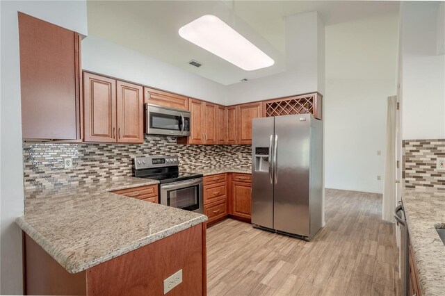1838 Eagle Ridge Blvd, Palm Harbor, FL 34685 - kitchen with appliances with stainless steel finishes, light wood-style flooring, brown cabinets, decorative backsplash, and a peninsula
