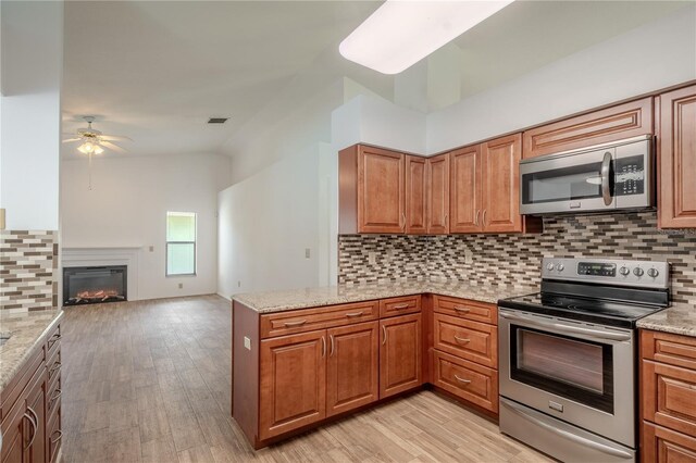 1838 Eagle Ridge Blvd, Palm Harbor, FL 34685 - kitchen with appliances with stainless steel finishes, a ceiling fan, backsplash, light stone countertops, and brown cabinetry