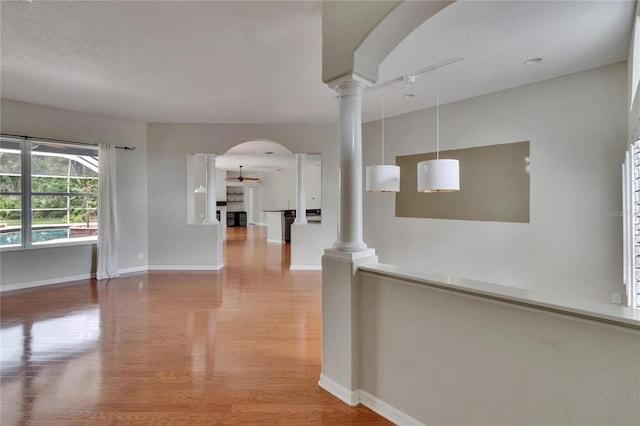27440 Cedar Park Ct, Wesley Chapel, FL 33544 - hallway featuring ornate columns, light wood-type flooring, rail lighting, arched walkways, and baseboards