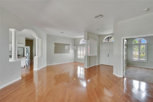 27440 Cedar Park Ct, Wesley Chapel, FL 33544 - unfurnished living room featuring decorative columns, healthy amount of natural light, light wood finished floors, baseboards, and a textured ceiling