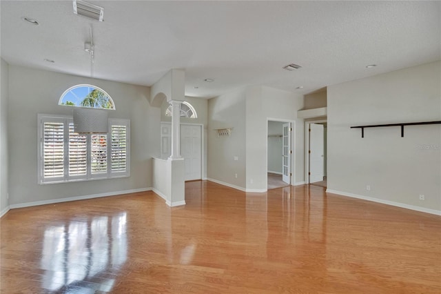 27440 Cedar Park Ct, Wesley Chapel, FL 33544 - empty room with ornate columns, light wood-type flooring, baseboards, a textured ceiling, and arched walkways