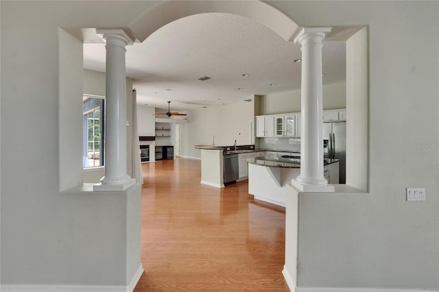 27440 Cedar Park Ct, Wesley Chapel, FL 33544 - kitchen with a peninsula, ornate columns, light wood finished floors, appliances with stainless steel finishes, and glass insert cabinets