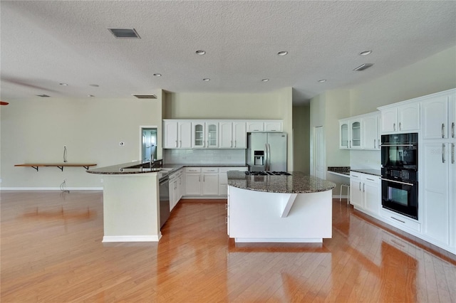 27440 Cedar Park Ct, Wesley Chapel, FL 33544 - kitchen with stainless steel appliances, a peninsula, light wood-style floors, glass insert cabinets, and decorative backsplash