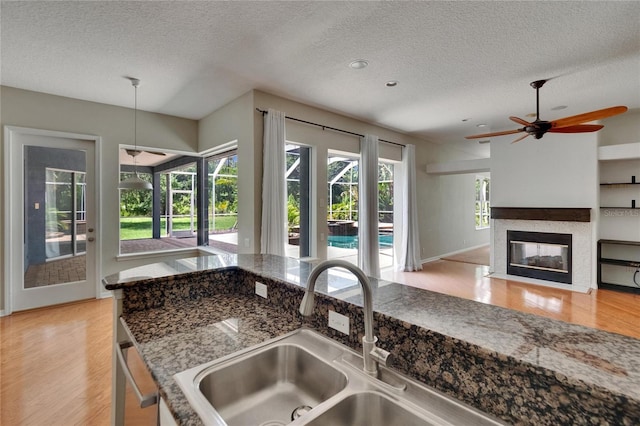 27440 Cedar Park Ct, Wesley Chapel, FL 33544 - kitchen with a textured ceiling, a sink, light wood-style flooring, ceiling fan, and a fireplace with flush hearth