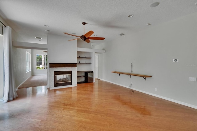 27440 Cedar Park Ct, Wesley Chapel, FL 33544 - unfurnished living room with a textured ceiling, light wood-style floors, ceiling fan, baseboards, and a multi sided fireplace