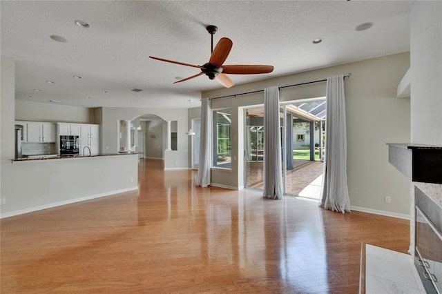 27440 Cedar Park Ct, Wesley Chapel, FL 33544 - unfurnished living room featuring arched walkways, light wood-style flooring, ceiling fan, baseboards, and a sink