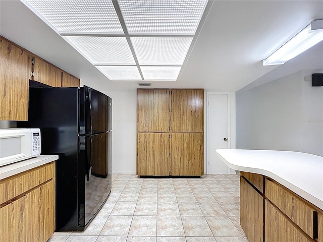 13725 Oak Forest Blvd N, Seminole, FL 33776 - kitchen with white microwave, light countertops, freestanding refrigerator, light tile patterned flooring, and brown cabinets