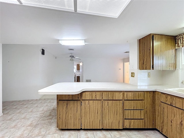 13725 Oak Forest Blvd N, Seminole, FL 33776 - kitchen featuring a peninsula, light countertops, brown cabinets, ceiling fan, and light tile patterned floors