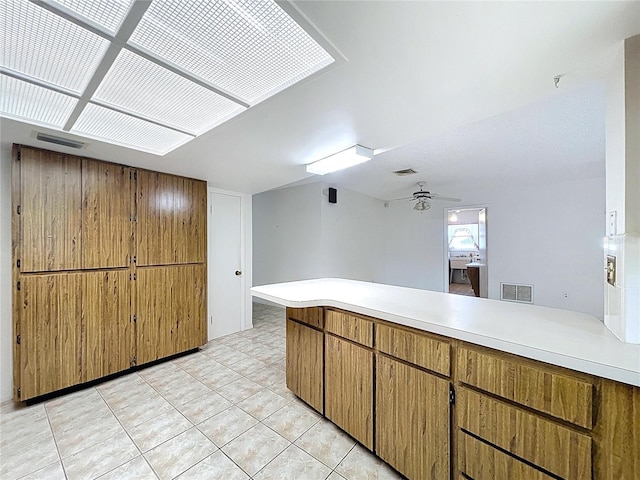 13725 Oak Forest Blvd N, Seminole, FL 33776 - kitchen with light countertops, a peninsula, light tile patterned flooring, brown cabinetry, and a ceiling fan