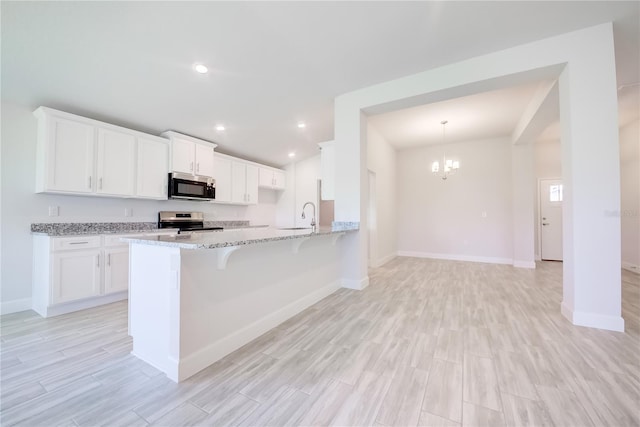 16508 66th Ln E, Parrish, FL 34219 - kitchen featuring appliances with stainless steel finishes, a chandelier, light stone counters, light wood-style floors, and a peninsula