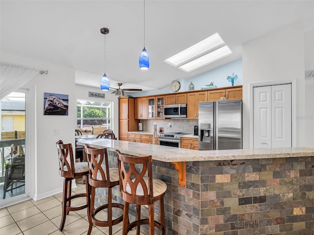 1102 Goshen Rd, Tarpon Springs, FL 34689 - kitchen with appliances with stainless steel finishes, brown cabinets, light tile patterned floors, vaulted ceiling, and backsplash
