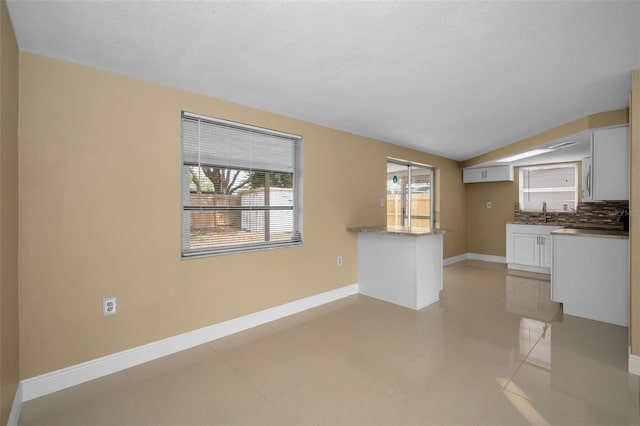 9100 Lunar Ln, Port Richey, FL 34668 - unfurnished living room featuring baseboards, a sink, vaulted ceiling, and light tile patterned floors