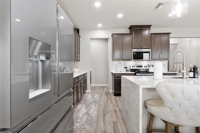 11719 Tetrafin Dr, Riverview, FL 33579 - kitchen with appliances with stainless steel finishes, light wood-style floors, dark brown cabinetry, backsplash, and a kitchen bar
