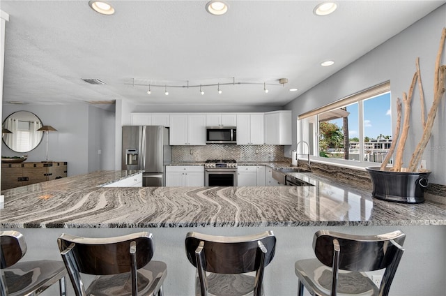 511 Island Way, Clearwater Beach, FL 33767 - kitchen with appliances with stainless steel finishes, stone countertops, white cabinets, a peninsula, and decorative backsplash