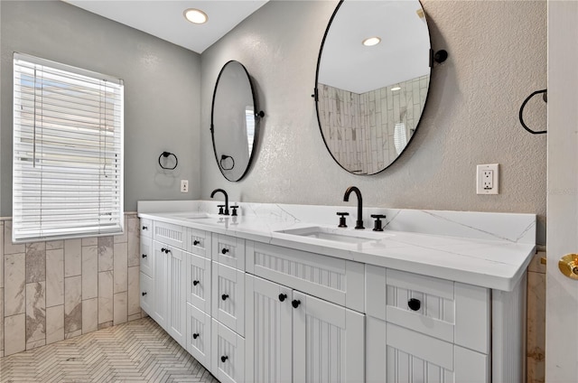 511 Island Way, Clearwater Beach, FL 33767 - full bathroom featuring double vanity, tile walls, healthy amount of natural light, a textured wall, and a wainscoted wall