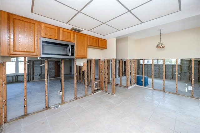 11465 7th St E, Treasure Island, FL 33706 - kitchen featuring stainless steel microwave, brown cabinetry, light tile patterned floors, and hanging light fixtures
