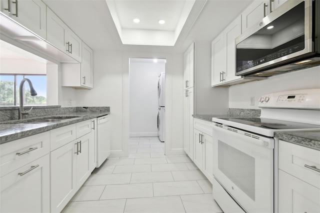 13612 S Village Dr Unit 5201, Tampa, FL 33618 - kitchen with white appliances, stacked washer / drying machine, a sink, recessed lighting, and white cabinetry