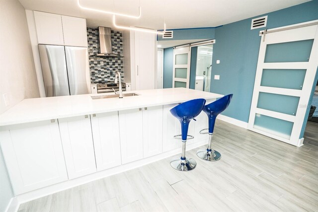 5712 Biscayne Ct Unit 201, New Port Richey, FL 34652 - kitchen featuring a barn door, wall chimney exhaust hood, stainless steel fridge, a sink, and backsplash