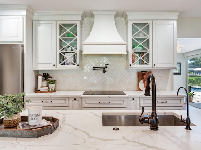 3724 Fawn Grove Ct, Land O Lakes, FL 34639 - kitchen with custom exhaust hood, black electric cooktop, freestanding refrigerator, and glass insert cabinets