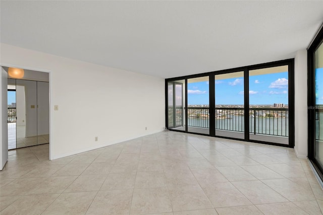 9425 Blind Pass Rd Unit 1008, St Pete Beach, FL 33706 - empty room with a water view, light tile patterned floors, healthy amount of natural light, a wall of windows, and baseboards