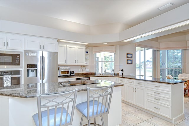 4304 Place Le Manes, Lutz, FL 33558 - kitchen with appliances with stainless steel finishes, a peninsula, light tile patterned floors, a sink, and white cabinetry