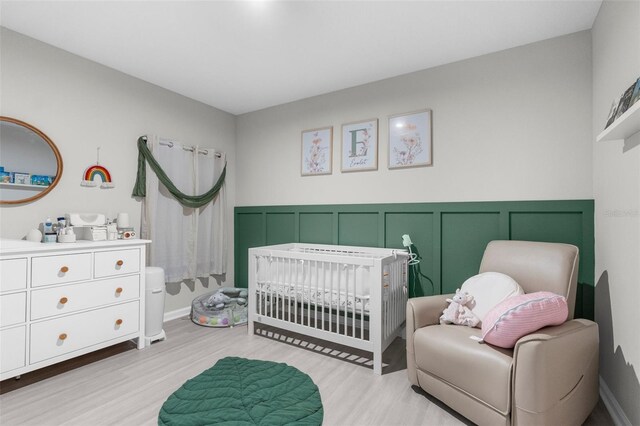 14532 Whitewater Way, Brooksville, FL 34604 - bedroom featuring a crib, light wood-style flooring, a decorative wall, and a wainscoted wall