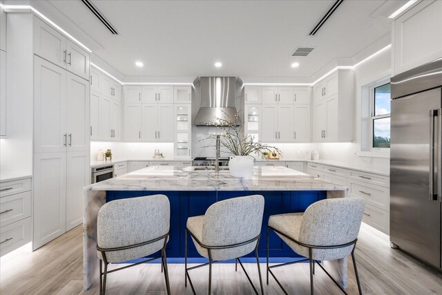 820 Bay Point Dr, Madeira Beach, FL 33708 - kitchen featuring stainless steel built in refrigerator, wall chimney range hood, white cabinetry, a kitchen bar, and light stone countertops