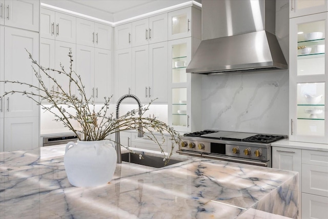 820 Bay Point Dr, Madeira Beach, FL 33708 - kitchen with wall chimney range hood, high end stove, decorative backsplash, white cabinetry, and glass insert cabinets