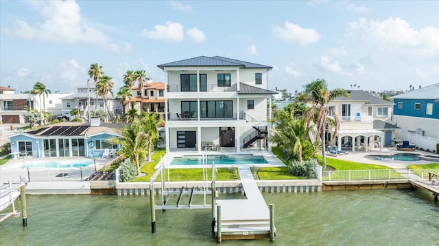 820 Bay Point Dr, Madeira Beach, FL 33708 - back of house with a balcony, an in-ground hot tub, a standing seam roof, an outdoor pool, and a patio area
