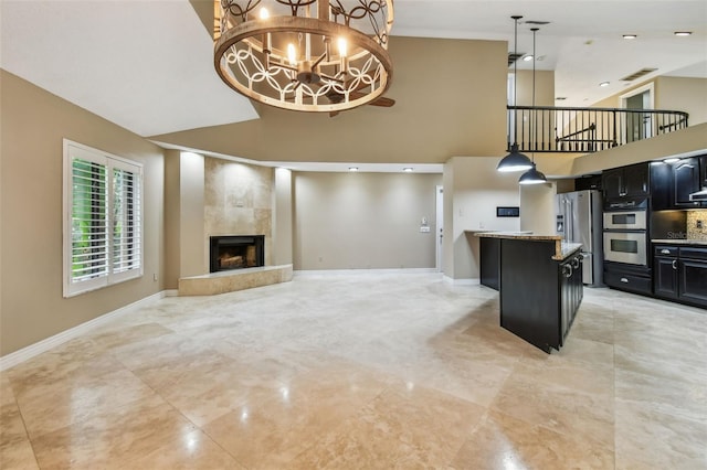 3308 Landing Pl, Palm Harbor, FL 34684 - kitchen featuring stainless steel appliances, a high ceiling, dark cabinetry, a fireplace with raised hearth, and baseboards