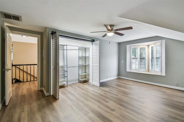 3308 Landing Pl, Palm Harbor, FL 34684 - unfurnished bedroom featuring wood finished floors, a barn door, baseboards, and ceiling fan