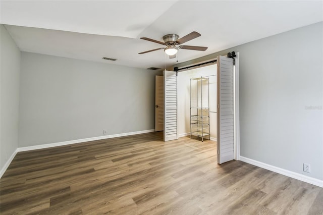 3308 Landing Pl, Palm Harbor, FL 34684 - unfurnished bedroom with wood finished floors, baseboards, a barn door, and a ceiling fan
