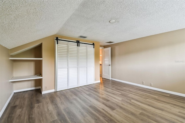 3308 Landing Pl, Palm Harbor, FL 34684 - unfurnished bedroom with a barn door, wood finished floors, a textured ceiling, baseboards, and vaulted ceiling