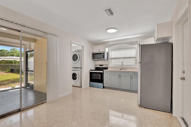 4714 W Vasconia St, Tampa, FL 33629 - kitchen featuring appliances with stainless steel finishes, stacked washing machine and dryer, dark speckled floor, gray cabinets, and light countertops