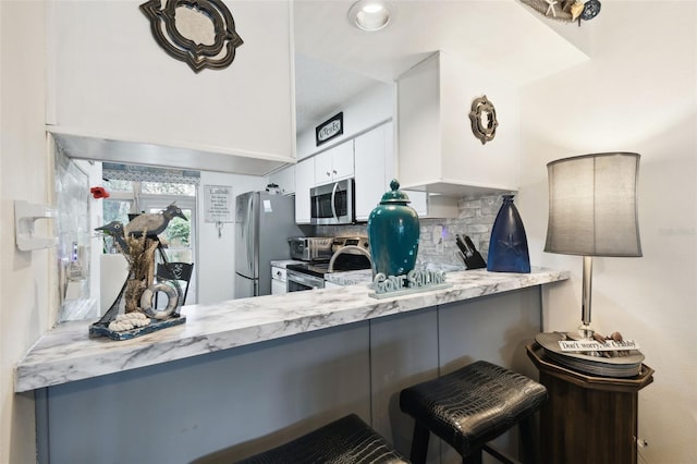 6630 Spring Flower Dr Unit 14, New Port Richey, FL 34653 - kitchen with appliances with stainless steel finishes, tasteful backsplash, white cabinetry, light stone countertops, and a breakfast bar area