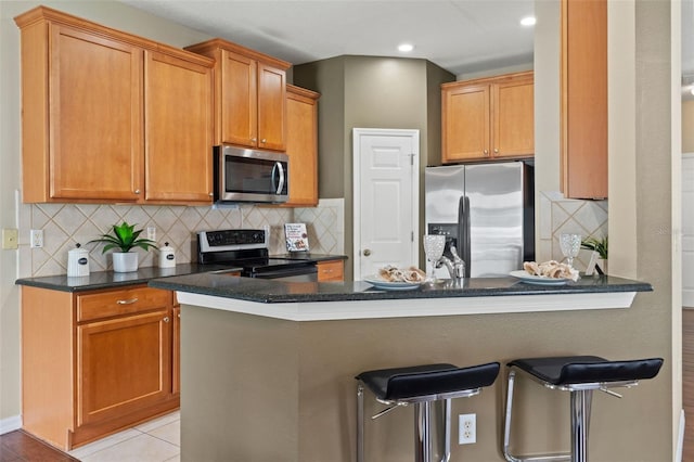 589 52nd Ave N, Saint Petersburg, FL 33703 - kitchen featuring stainless steel appliances, a peninsula, a breakfast bar, tasteful backsplash, and dark stone countertops