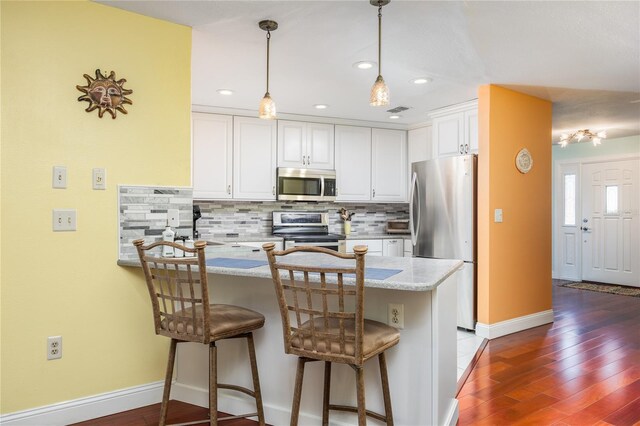 460 Meravan Dr, Palm Harbor, FL 34683 - kitchen with appliances with stainless steel finishes, a peninsula, white cabinets, tasteful backsplash, and wood finished floors