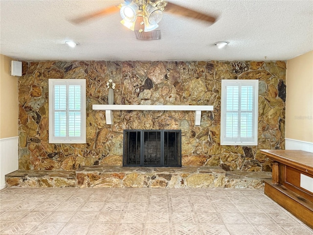 2523 Krueger Ln, Tampa, FL 33618 - unfurnished living room featuring a textured ceiling, a ceiling fan, plenty of natural light, a stone fireplace, and wainscoting