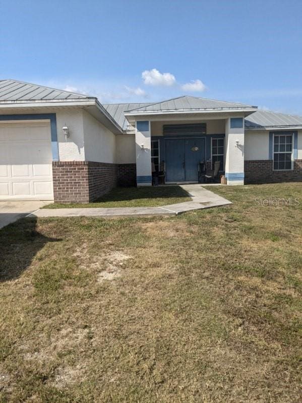 9761 Councilor Ln, North Fort Myers, FL 33917 - rear view of property featuring brick siding, metal roof, a standing seam roof, a lawn, and stucco siding