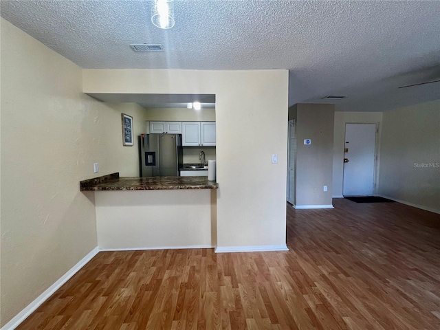 4215 E Bay Dr Unit 1707C, Clearwater, FL 33764 - kitchen with stainless steel refrigerator with ice dispenser, baseboards, wood finished floors, a textured ceiling, and white cabinets