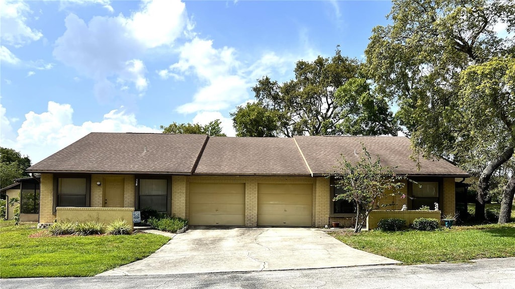 502 E Curlew Pl, Tarpon Springs, FL 34689 - view of front of house with brick siding, a garage, driveway, a front yard, and roof with shingles