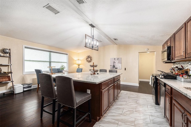9220 Mcintosh Rd, Dover, FL 33527 - kitchen with a breakfast bar area, vaulted ceiling, appliances with stainless steel finishes, a kitchen island, and light stone counters