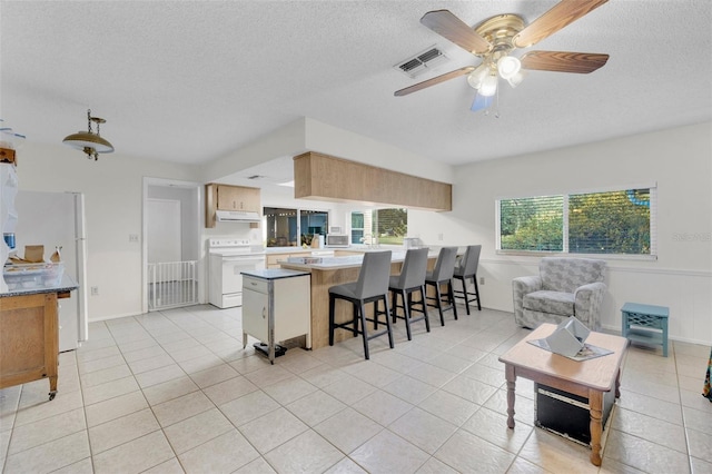 7708 Fairlawn Dr, Hudson, FL 34667 - kitchen with white appliances, under cabinet range hood, light tile patterned flooring, a textured ceiling, and a ceiling fan