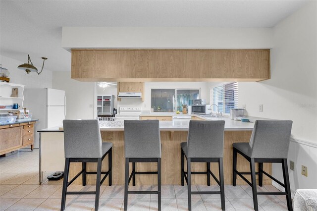 7708 Fairlawn Dr, Hudson, FL 34667 - kitchen with white appliances, a peninsula, a kitchen bar, a sink, and light countertops