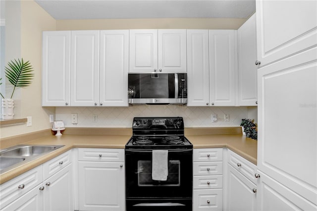 4221 W Spruce St Unit 1429, Tampa, FL 33607 - kitchen featuring stainless steel microwave, black range with electric stovetop, white cabinets, and decorative backsplash