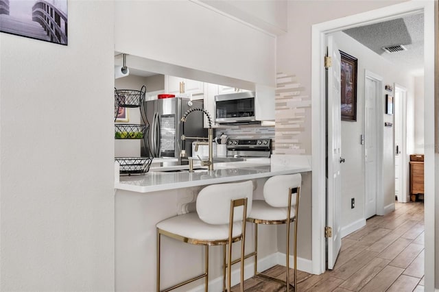 2824 Paddock Dr, Palm Harbor, FL 34684 - kitchen with stainless steel appliances, tasteful backsplash, light wood-style flooring, white cabinetry, and a breakfast bar area