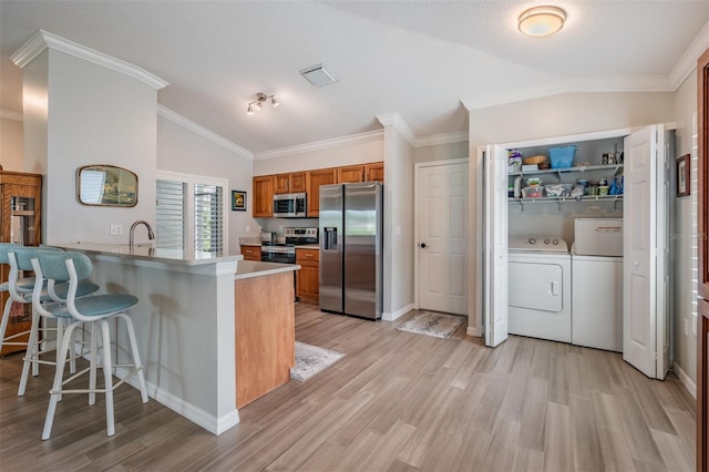 10232 Buncombe Way, San Antonio, FL 33576 - kitchen featuring stainless steel appliances, washer and clothes dryer, brown cabinets, vaulted ceiling, and light wood-style flooring